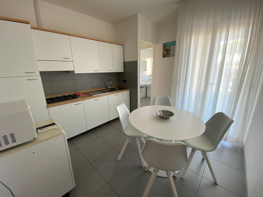 a white kitchen with a white table and chairs at Appartamenti al Cigno in Lignano Sabbiadoro