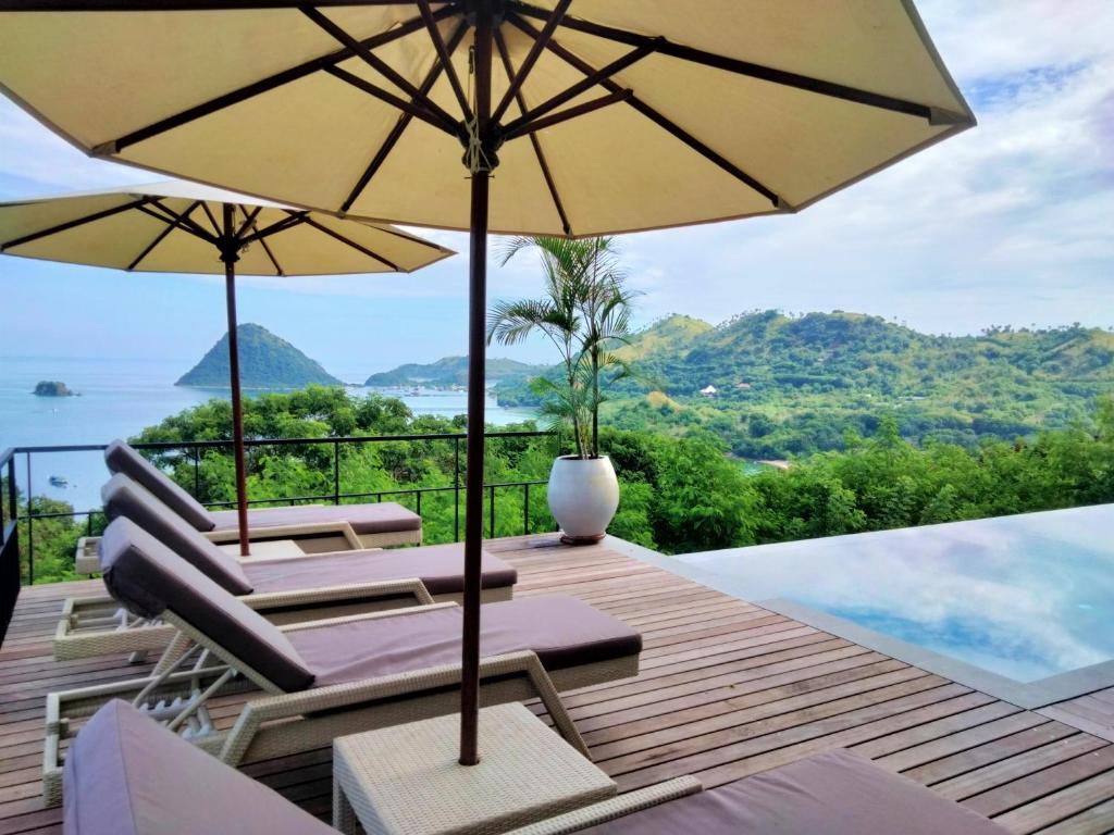 una terraza con sillas y sombrillas y una piscina en Paradise Garage Komodo Villa, en Labuan Bajo