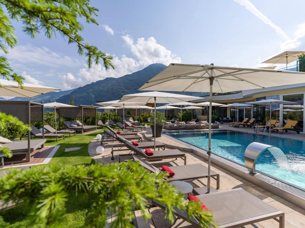 una piscina al aire libre con mesas, sillas y sombrillas en Platzlhof - Mein Hotel im Zillertal, en Ried im Zillertal