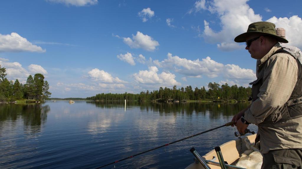 a man is standing in a boat with a fishing pole at Wilderness Hotel Nellim & Igloos in Inari