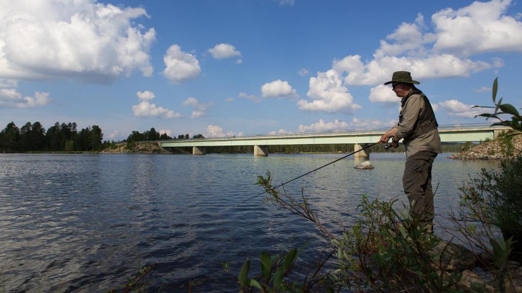 a man is standing in the water with a fishing rod at Wilderness Hotel Nellim & Igloos in Inari