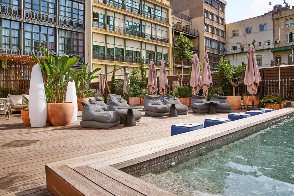 einen Pool mit Stühlen und Sonnenschirmen neben einem Gebäude in der Unterkunft ICON Bcn in Barcelona
