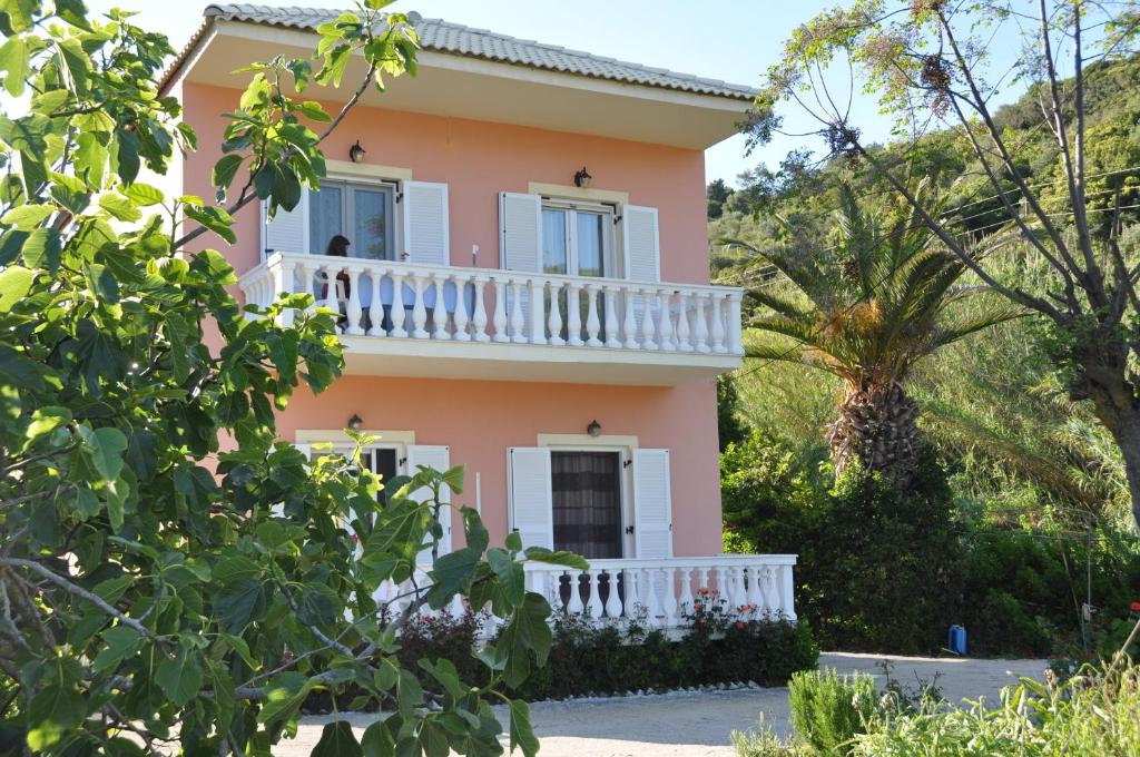 Casa rosa con balcón blanco y árboles en Villa Vasiliki, en Vitalades