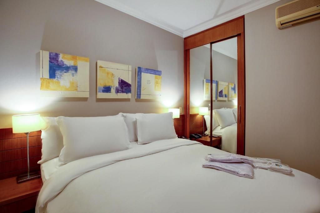 1 dormitorio con 1 cama grande con sábanas y almohadas blancas en Roomo Bela Cintra Residencial, en São Paulo