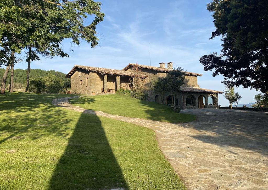 an old stone house with a long shadow on the grass at Masia Santa Llúcia in Rupit