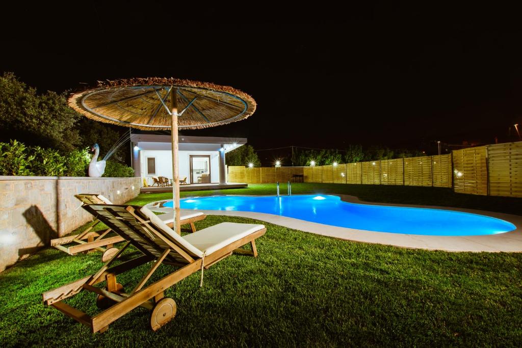 卡尼亞鎮的住宿－Chania Oasis with heated pool，夜间游泳池,配有椅子和遮阳伞