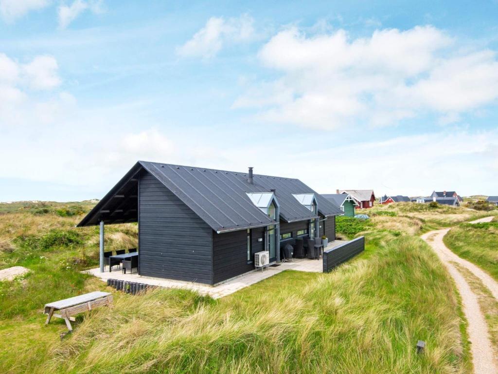 a black house on the beach with a bench at 6 person holiday home in R m in Bolilmark