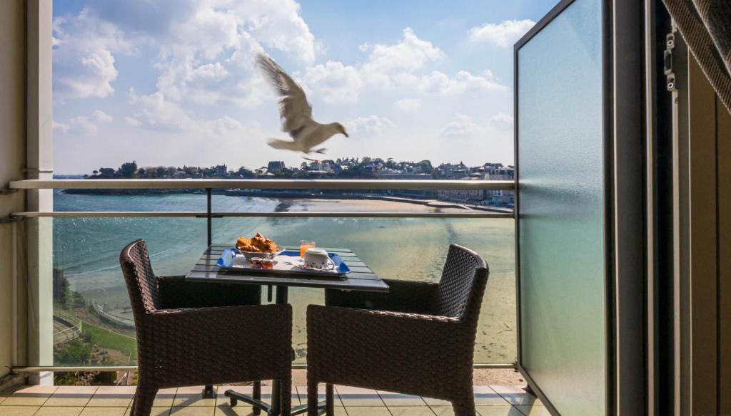 um pássaro a voar sobre uma mesa com comida numa varanda em Le Crystal Dinard Plage em Dinard