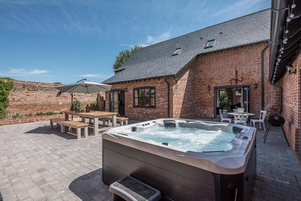una vasca idromassaggio su un patio accanto a un edificio in mattoni di Chapel Cottage at Pond Hall Farm, Stunnning Property with Private Hot Tub, Hadleigh a Ipswich
