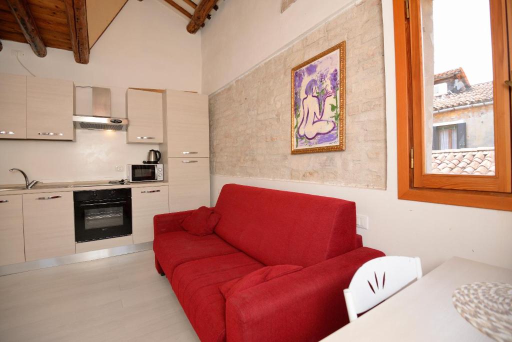 um sofá vermelho numa sala de estar com uma cozinha em Casa dea corte apartment em Veneza
