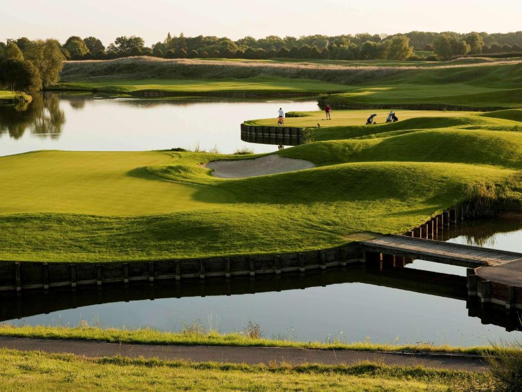 un campo da golf con ponte su un laghetto di Novotel Saint-Quentin en Yvelines a Magny-les-Hameaux