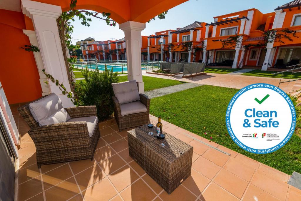 a patio with chairs and an umbrella with the clean and safe logo at Anis Lux Tavira Residence Villa 5Q in Luz de Tavira
