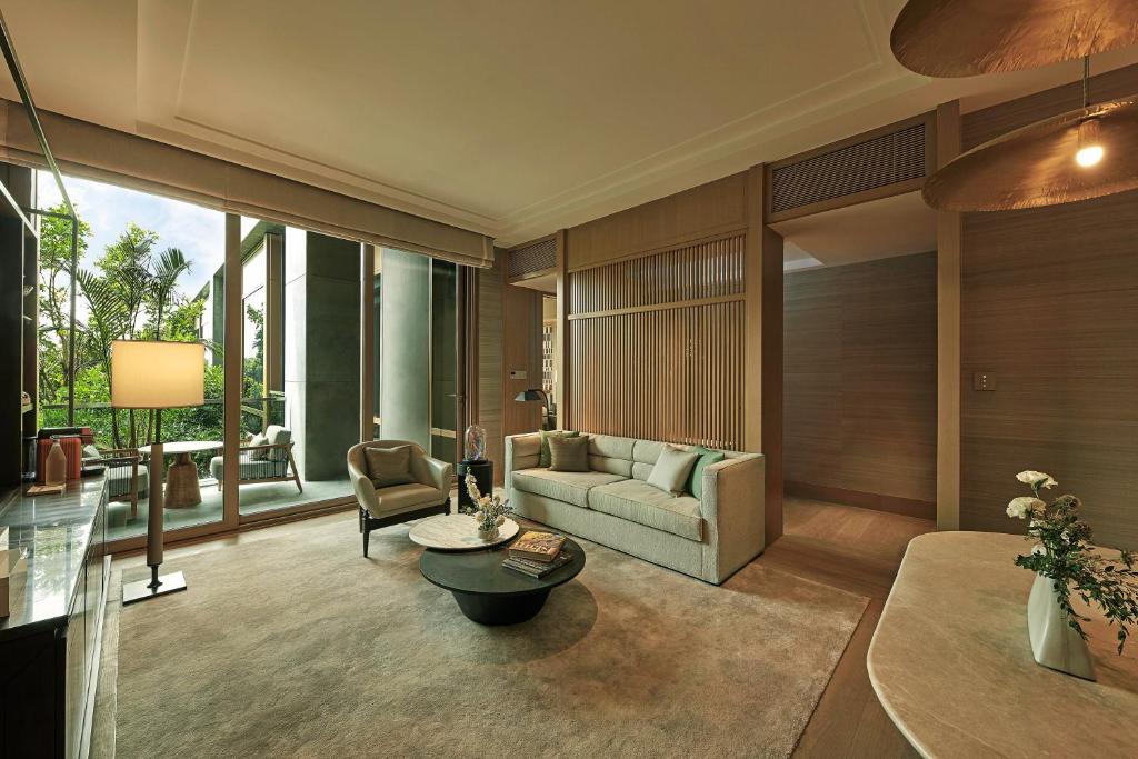A refined suite sitting room with a sofa, armchairs, and full-height glass doors opening toward greenery.