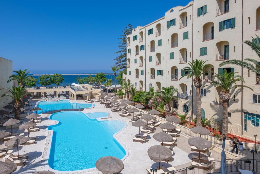 ośrodek z basenem, krzesłami i budynkiem w obiekcie Hotel Hopps w mieście Mazara del Vallo