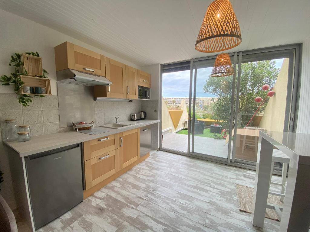 une cuisine avec des placards en bois et une grande fenêtre dans l'établissement Cap D'agde Naturiste Heliopolis 2 à 4 Personnes Appartement OSMOSE, au Cap d'Agde