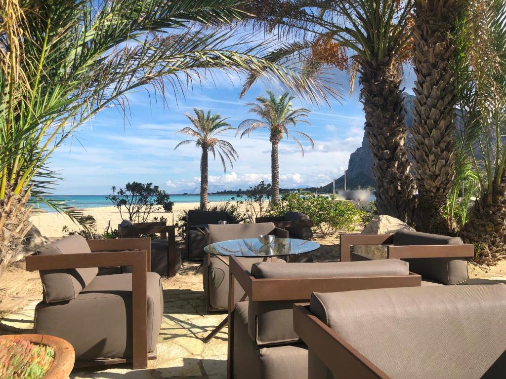 a beach with chairs and a table and palm trees at Hotel Capo San Vito by Geocharme in San Vito lo Capo