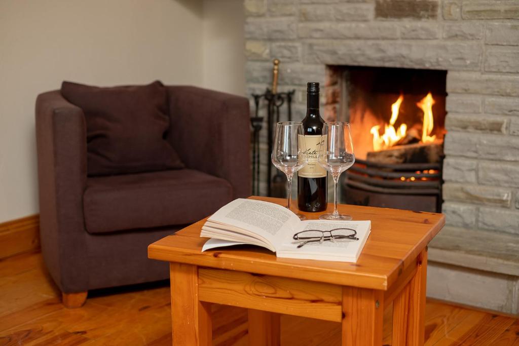 a table with a book and wine glasses and a fireplace at Piper's Chair Houses in Doolin