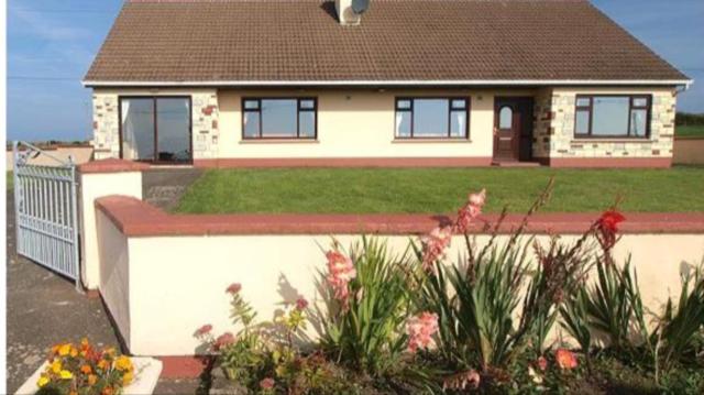 uma casa com uma cerca e um quintal com flores em The Bungalow em Doonbeg