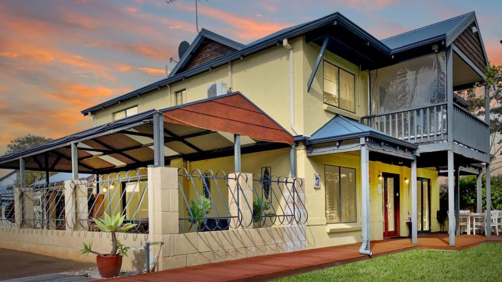 a yellow house with a balcony with surfboards on it at Observatory Guesthouse - Adults Only in Busselton