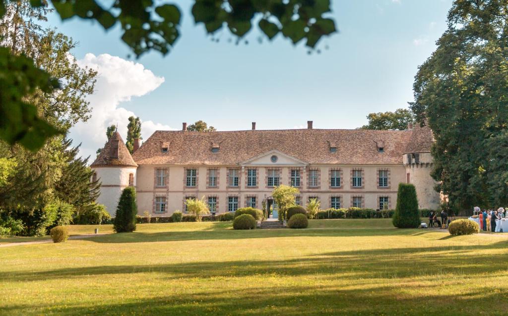 Château de la Cour Senlisse في Senlisse: منزل كبير على حقل عشبي مع أشخاص يسيرون حوله