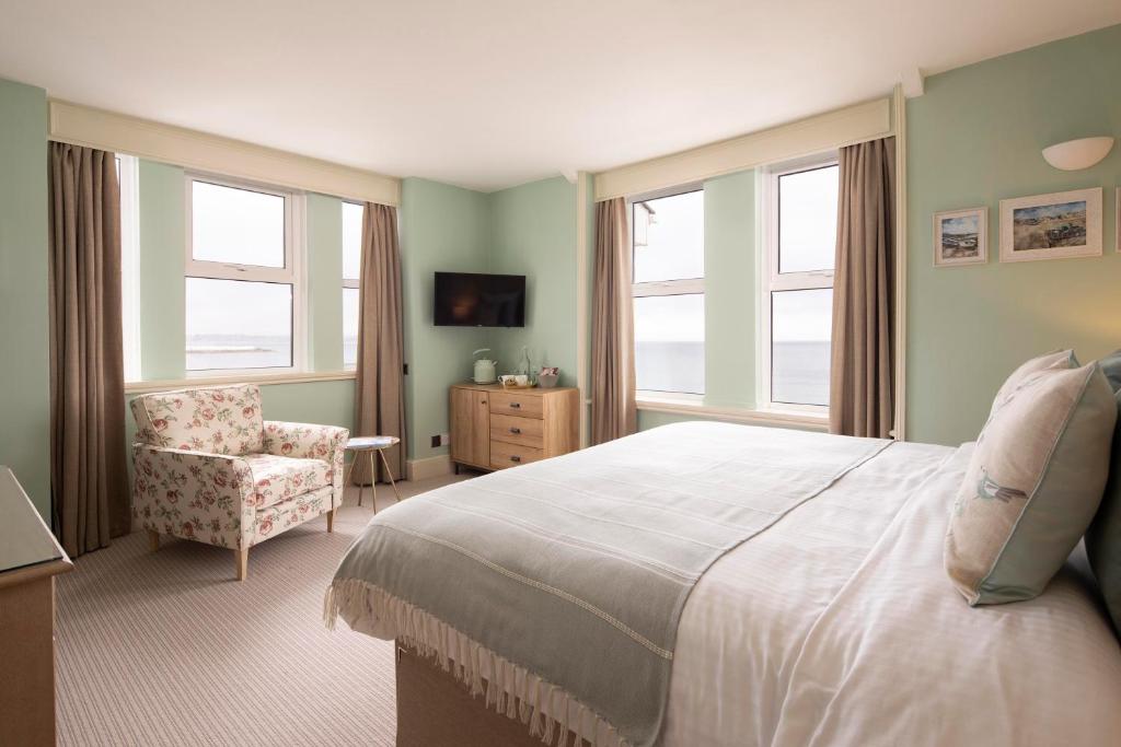 a bedroom with a bed and a chair and windows at The Beach Club in Penzance