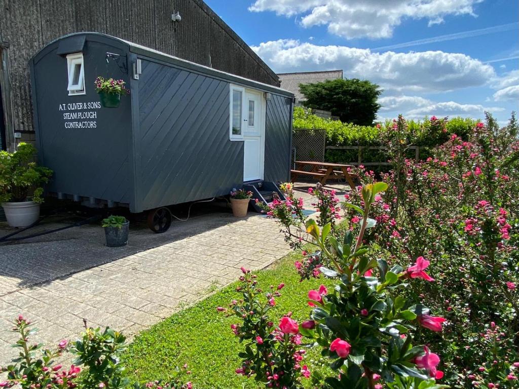 a tiny house in a garden with flowers at Shepherd's Hut at Puttocks Farm in Great Dunmow