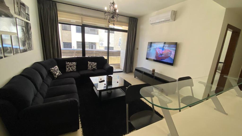 a living room with a black couch and a glass table at Dair Ghbar Apartment in Amman