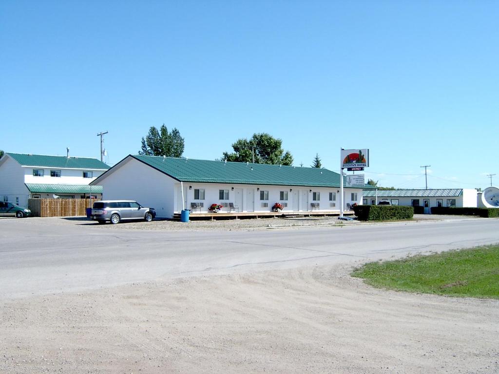 a white building with a car parked in a parking lot at Sundown Motel in Watrous