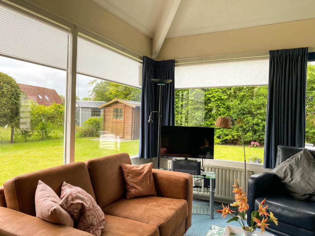 a living room with a couch and a tv and windows at Hello Zeeland - Vakantiehuis Duinroos 181 in Breskens