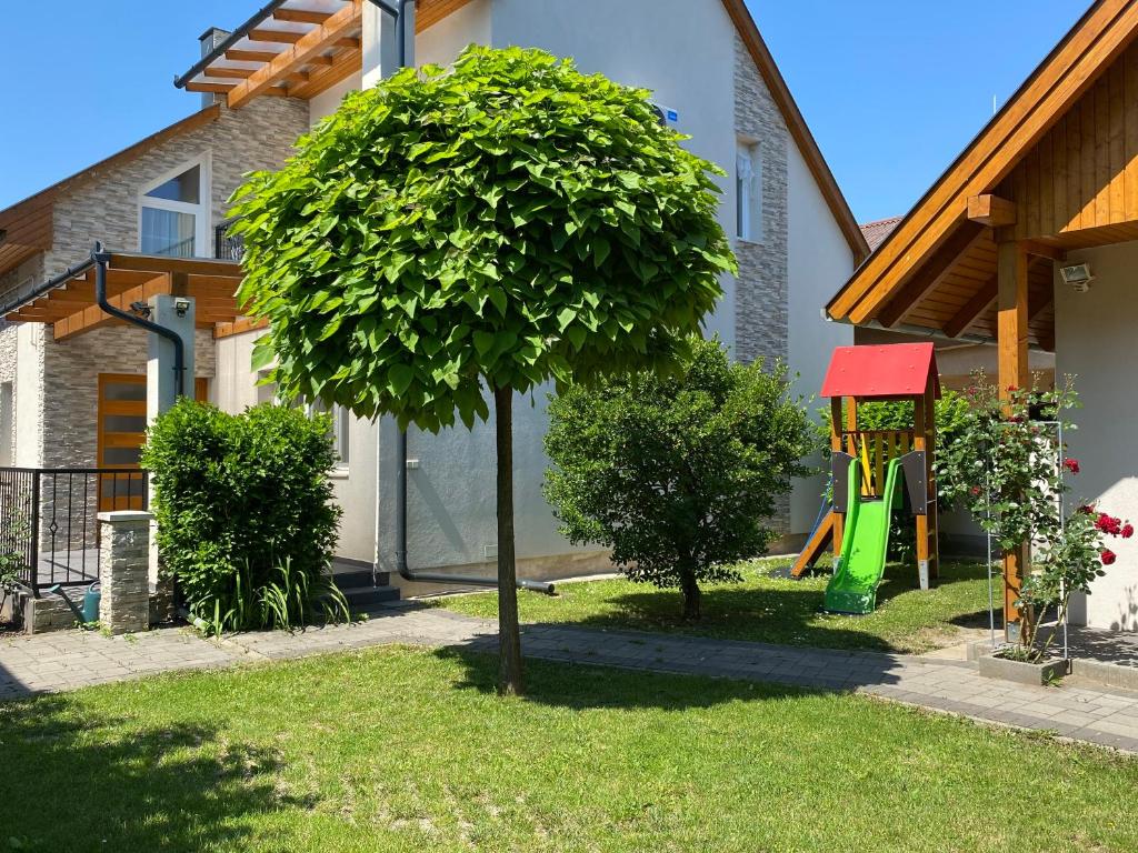 ein Baum vor einem Haus mit Spielplatz in der Unterkunft Magyar Apartman III. in Hajdúszoboszló