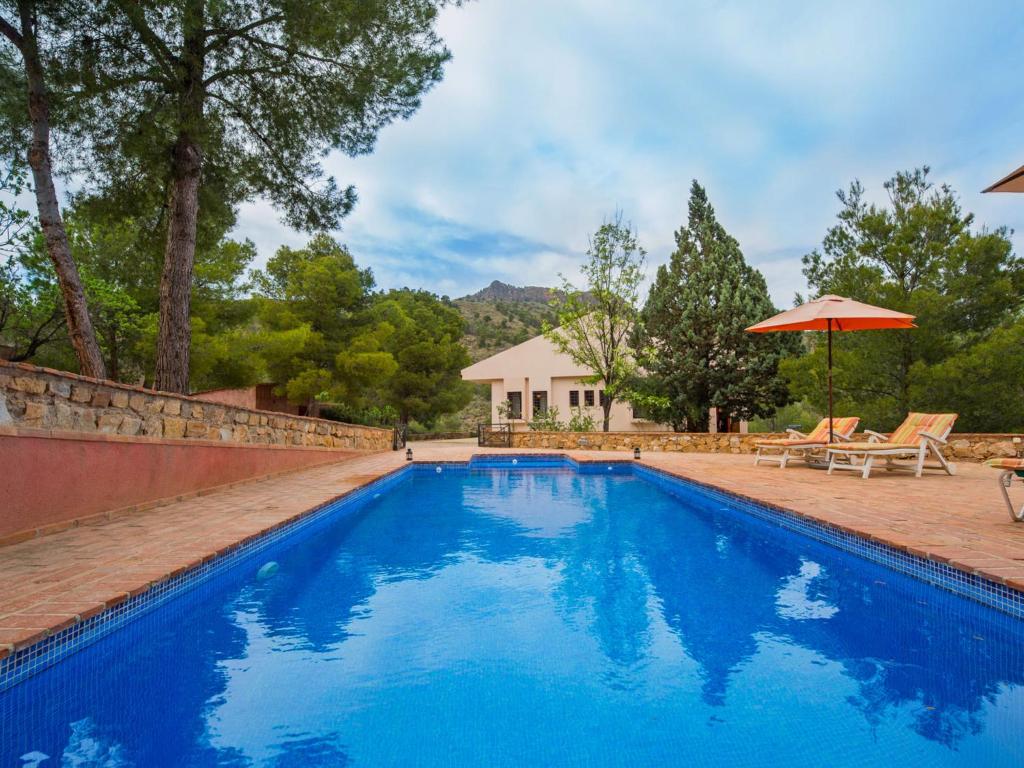 a blue swimming pool with an umbrella and a house at Holiday Home De la Cruz by Interhome in Aledo