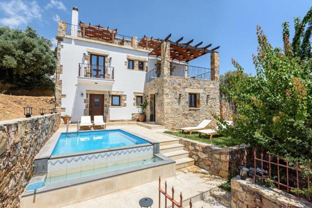 a villa with a swimming pool in front of a house at Minos Country Living Apartments in Agrilés
