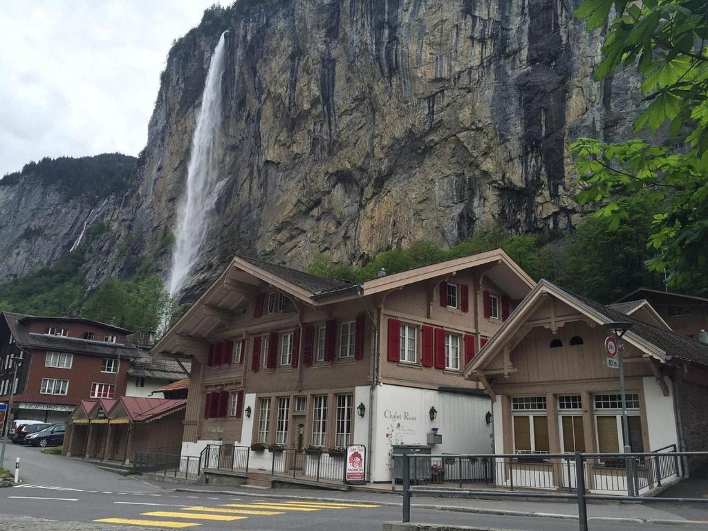 a building with a waterfall in front of a mountain at Chalet Rosa B&B in Lauterbrunnen