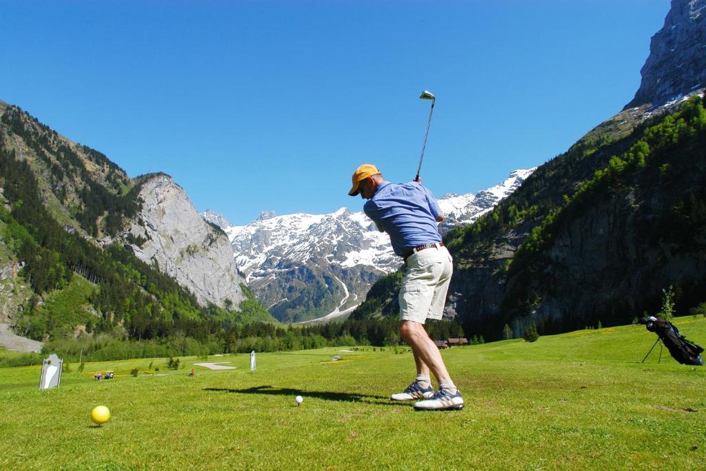 a man playing golf in a field with mountains at Hotel Central in Engelberg