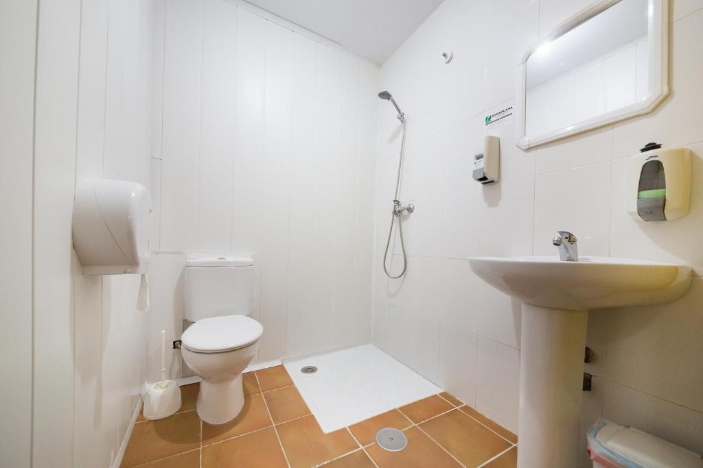 La salle de bains blanche est pourvue de toilettes et d'un lavabo. dans l'établissement Albergue Villa San Clemente, à Tui