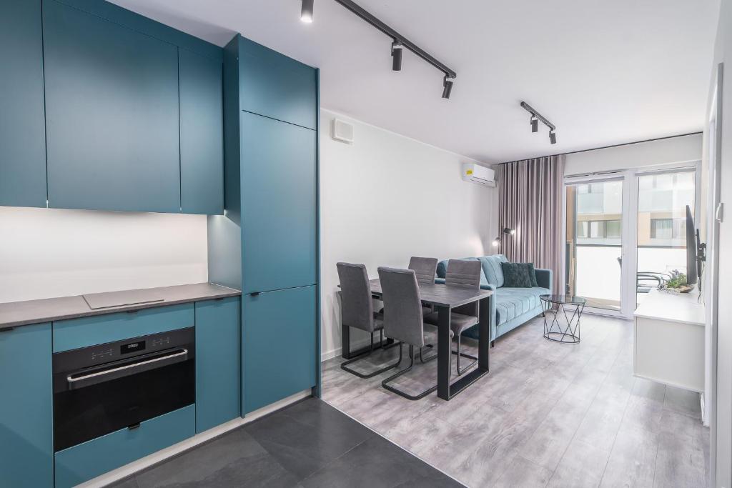 a kitchen and dining room with blue cabinets and a table at Green Sea Apartamenty Kasprowicza in Kołobrzeg