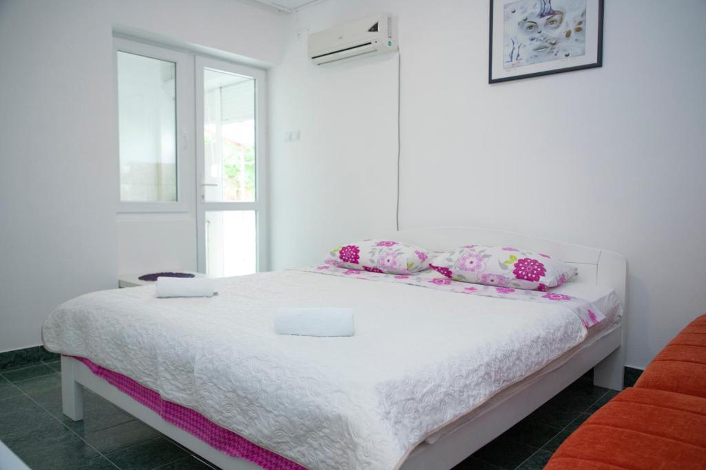 a white bedroom with a white bed with pink pillows at 4 Studios Becic in Budva