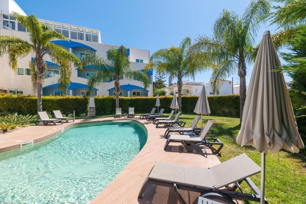 uma piscina com cadeiras e guarda-sóis ao lado de um edifício em Velamar Boutique Hotel - Adults Friendly em Albufeira