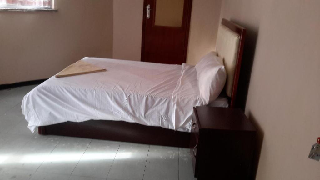 um quarto com uma cama com lençóis brancos e uma mesa em Rediet Pension em Addis Ababa