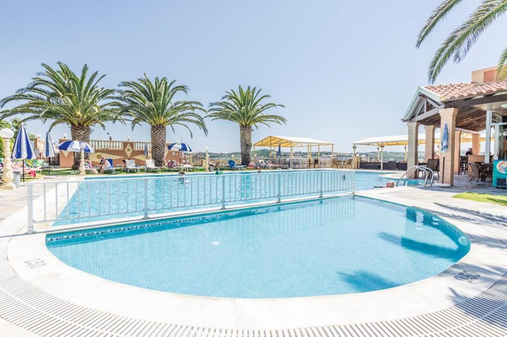 a large swimming pool with palm trees in a resort at Kapetanios Apartments in Agios Stefanos