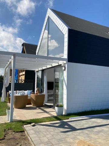 a white house with a person sitting in a chair at Domek z jacuzzi Summer House Dziwnówek Wrzosowo in Wrzosowo