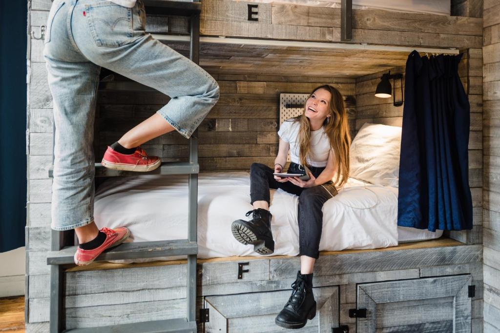 a woman sitting on a bunk bed with a person standing on a ladder at Hostel Fish in Denver