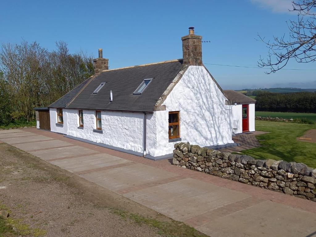 une maison blanche avec un mur en pierre devant elle dans l'établissement Meikle Aucheoch Holiday Cottage, plus Hot Tub, Near Maud, in the heart of Aberdeenshire, à Peterhead
