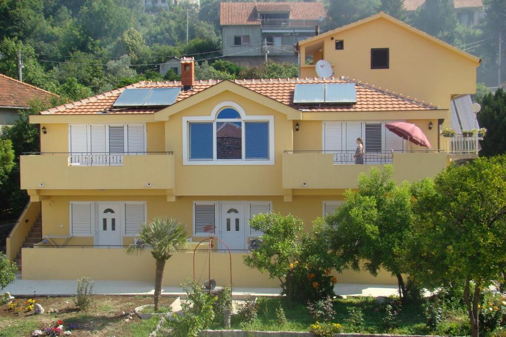 a yellow house with a woman on the balcony at Apartment Diana in Tivat