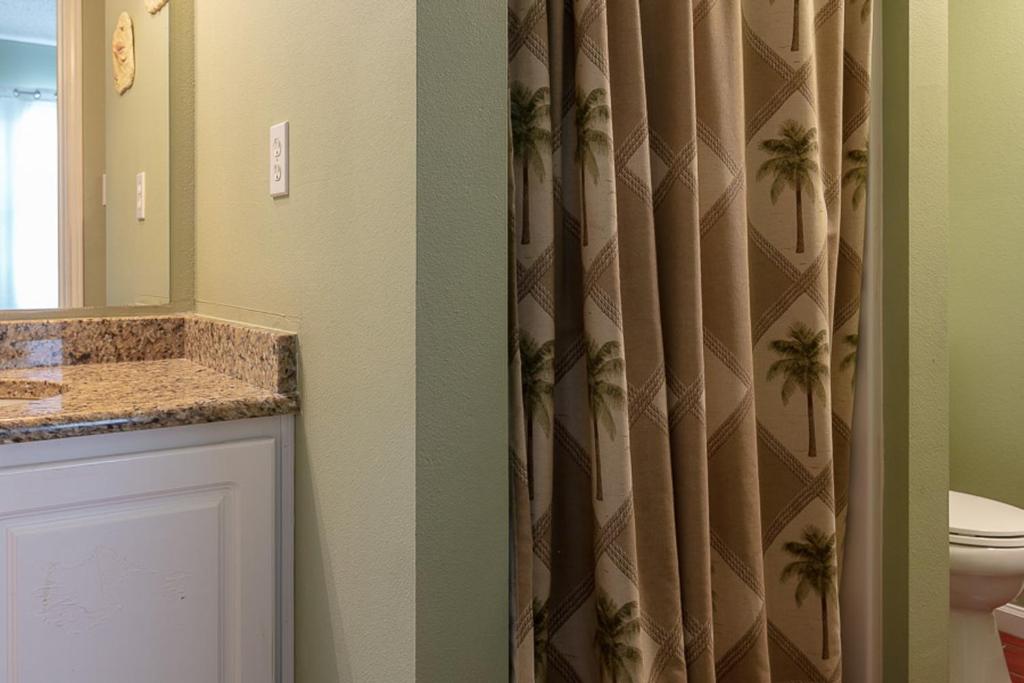 a bathroom with a toilet and a shower curtain with palm trees at Tropic Isl 501 in Gulf Shores
