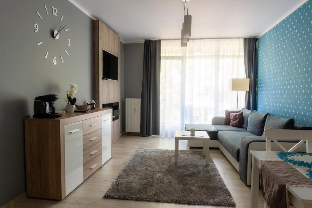 a living room with a couch and a clock on the wall at Apartamenty Brzask-Dawn, Bryza-Breeze - Osiedle Polanki in Kołobrzeg