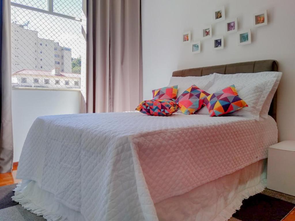 Un dormitorio con una cama rosa con almohadas y una ventana en Ensolarado ao lado do shopping com garagem e Wifi en Teresópolis
