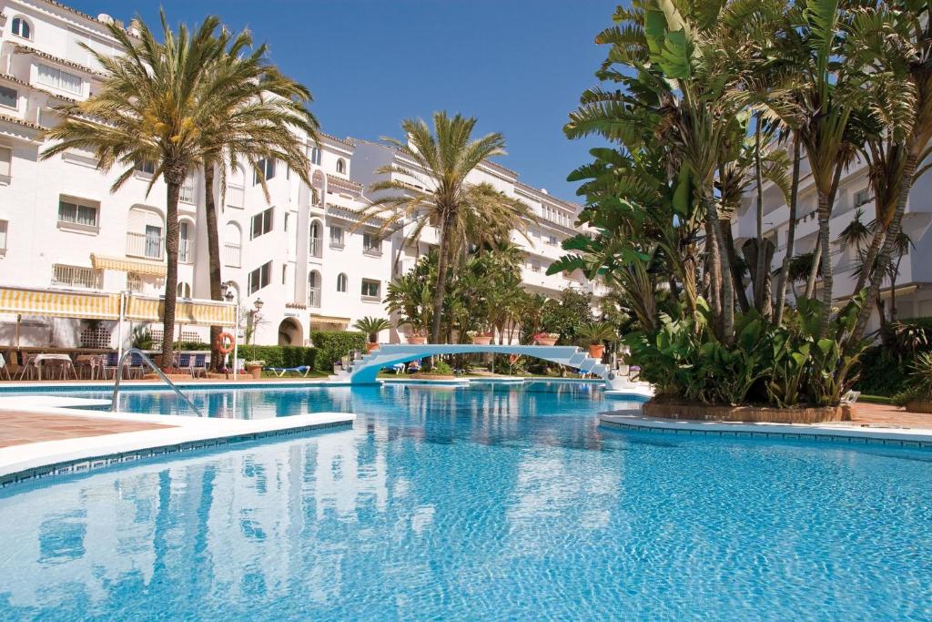 a large swimming pool with palm trees and buildings at Playa Real in Marbella