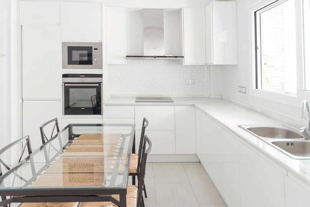 cocina blanca con mesa de cristal y fregadero en Unik Apartment Alicante, en Alicante