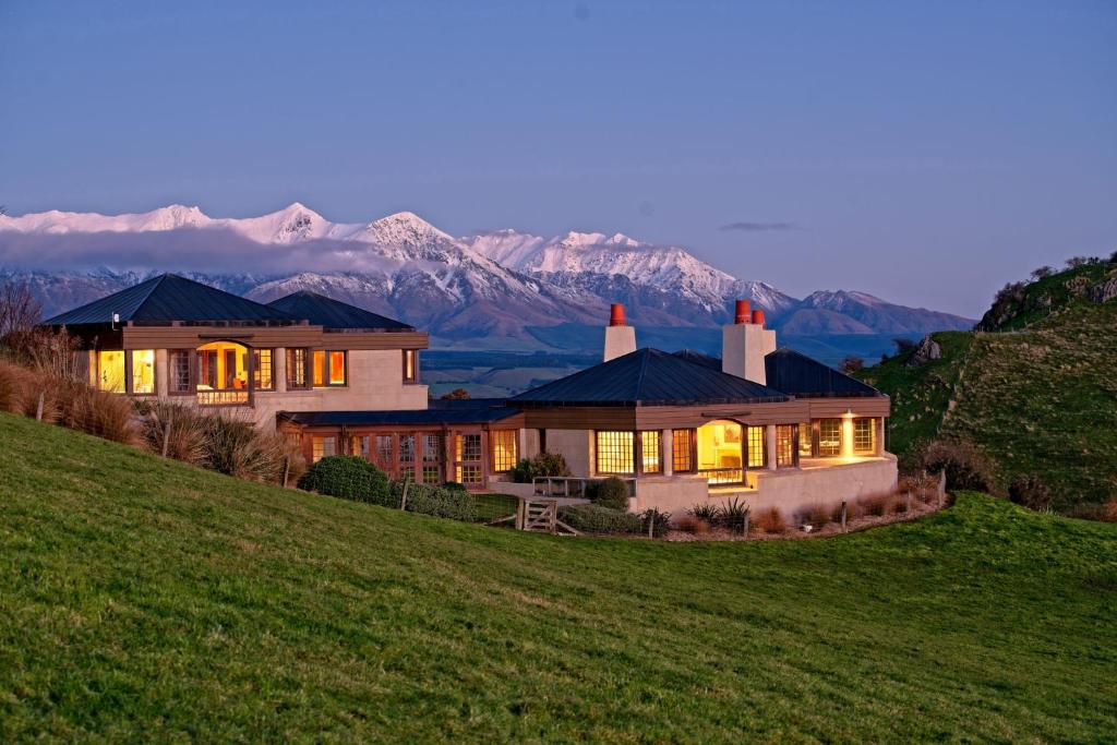 une maison sur une colline avec des montagnes en arrière-plan dans l'établissement Cabot Lodge - Fiordland National Park, à Manapouri